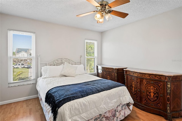 bedroom with light wood-type flooring, ceiling fan, a textured ceiling, and baseboards