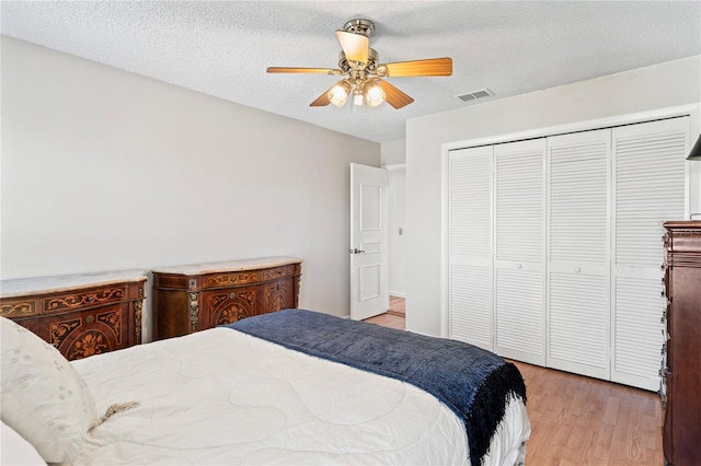 bedroom featuring light wood finished floors, a closet, visible vents, a ceiling fan, and a textured ceiling