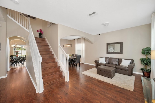 living room with dark wood-type flooring, arched walkways, visible vents, and stairs