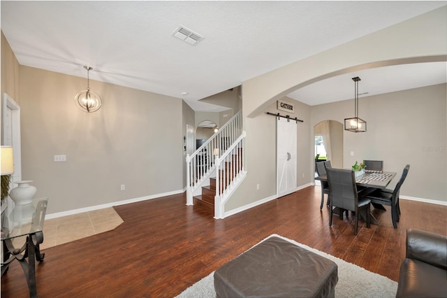 living room featuring arched walkways, visible vents, a barn door, wood finished floors, and baseboards