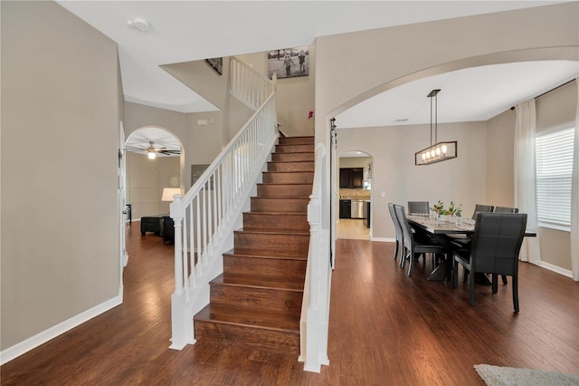 stairway featuring baseboards, arched walkways, and wood finished floors