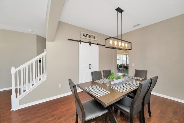 dining room with wood finished floors, visible vents, baseboards, and a barn door