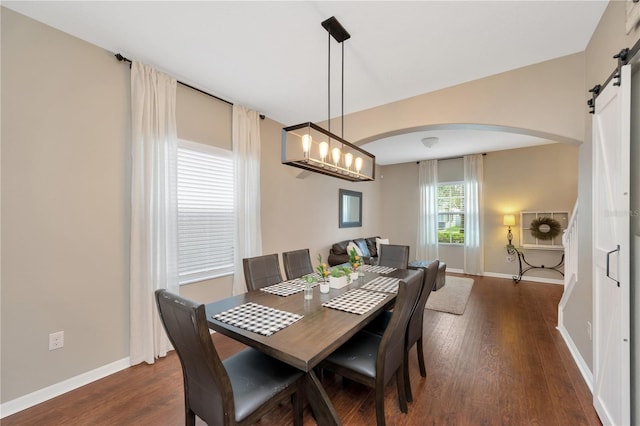 dining area with arched walkways, a barn door, wood finished floors, and baseboards