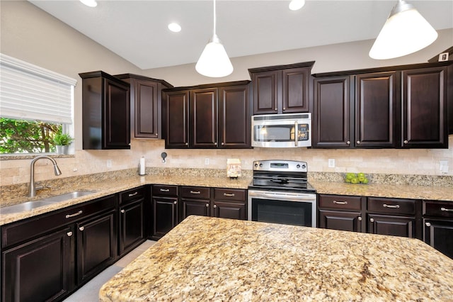 kitchen with hanging light fixtures, a sink, light stone countertops, stainless steel appliances, and backsplash