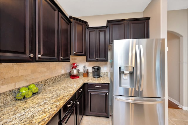 kitchen with tasteful backsplash, light stone countertops, dark brown cabinetry, and stainless steel fridge with ice dispenser