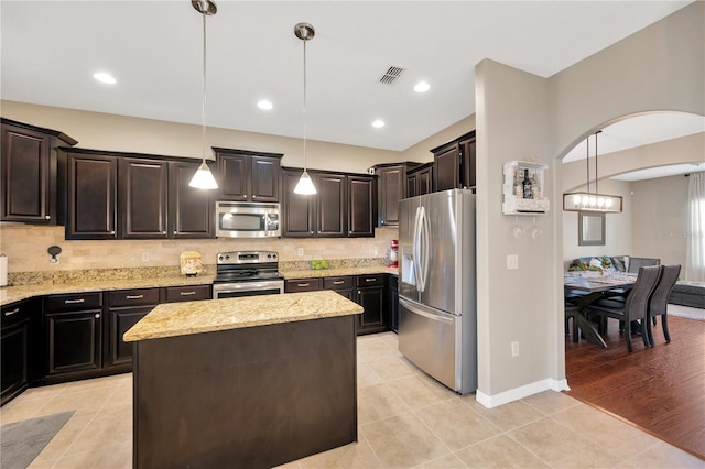 kitchen with a kitchen island, appliances with stainless steel finishes, light stone counters, backsplash, and light tile patterned flooring