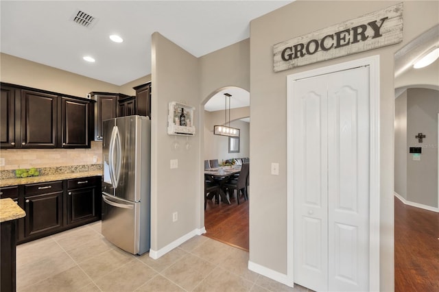 kitchen with arched walkways, light tile patterned floors, visible vents, tasteful backsplash, and stainless steel fridge