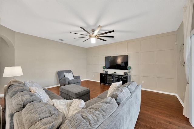 living area featuring arched walkways, dark wood-style flooring, a ceiling fan, and a decorative wall