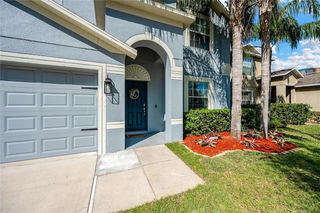 entrance to property featuring a garage, a lawn, and stucco siding