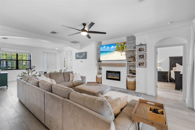 living area with light wood-type flooring, visible vents, ornamental molding, a large fireplace, and a decorative wall