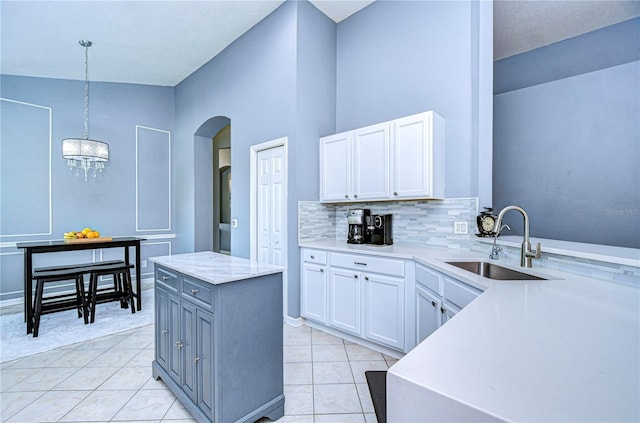 kitchen featuring arched walkways, decorative light fixtures, decorative backsplash, white cabinetry, and a sink