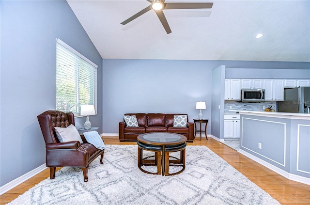 living room with vaulted ceiling, light wood-style flooring, baseboards, and ceiling fan