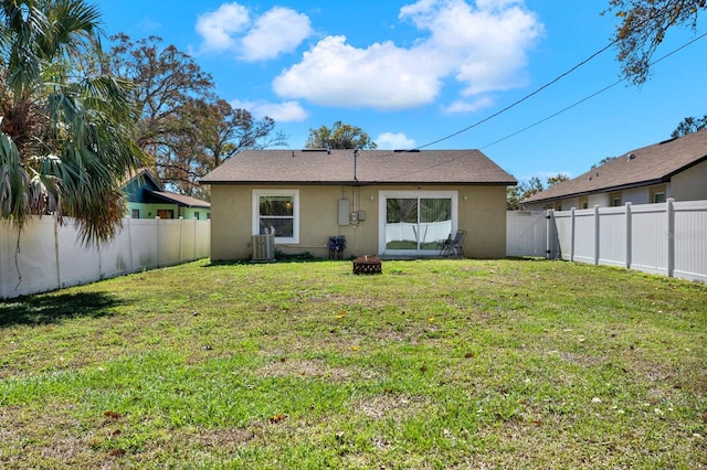 rear view of house featuring a yard, central AC unit, a fenced backyard, and stucco siding