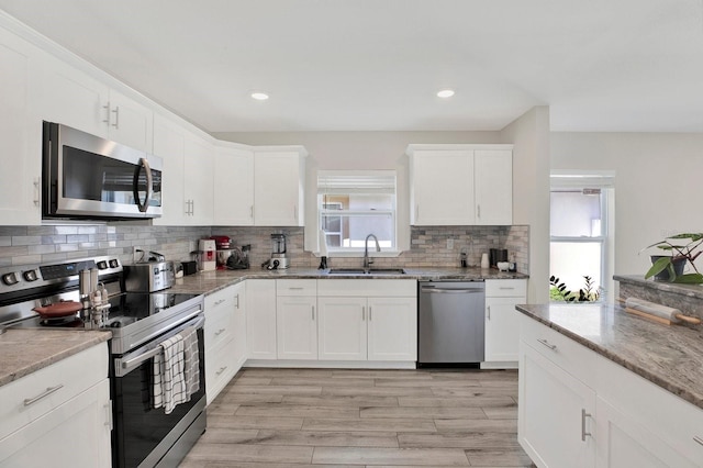 kitchen featuring light stone counters, stainless steel appliances, decorative backsplash, white cabinetry, and a sink