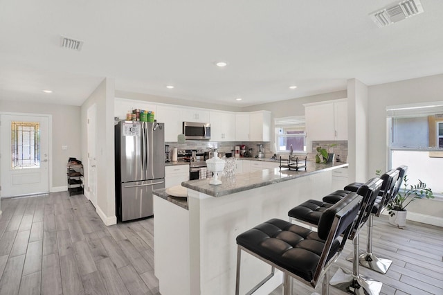 kitchen with visible vents, appliances with stainless steel finishes, decorative backsplash, and a kitchen breakfast bar