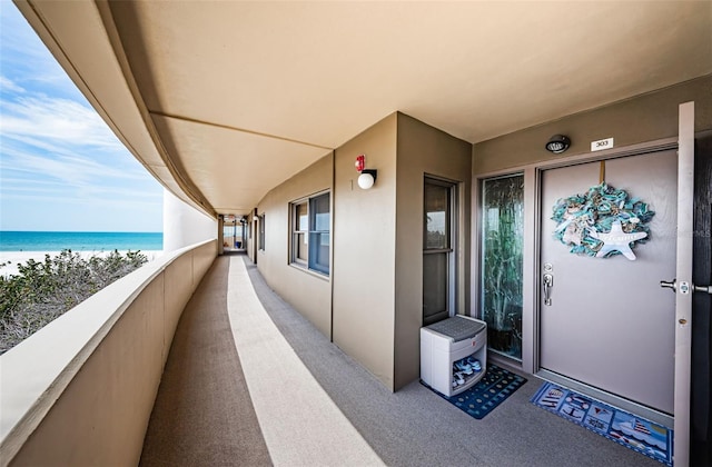 property entrance with a beach view, a balcony, a water view, and stucco siding