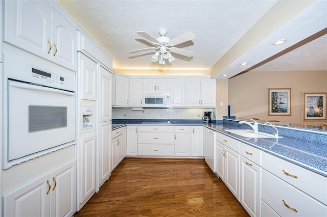 kitchen with white appliances, wood finished floors, a sink, a textured ceiling, and white cabinetry