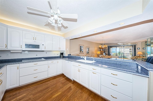 kitchen featuring a sink, wood finished floors, open floor plan, white cabinetry, and white appliances