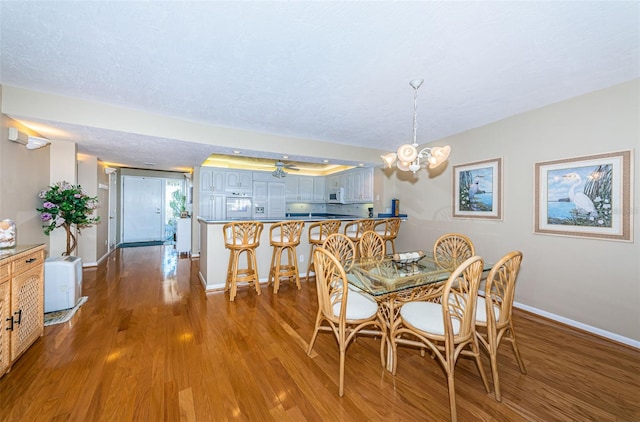 dining space featuring an inviting chandelier, wood finished floors, baseboards, and a textured ceiling