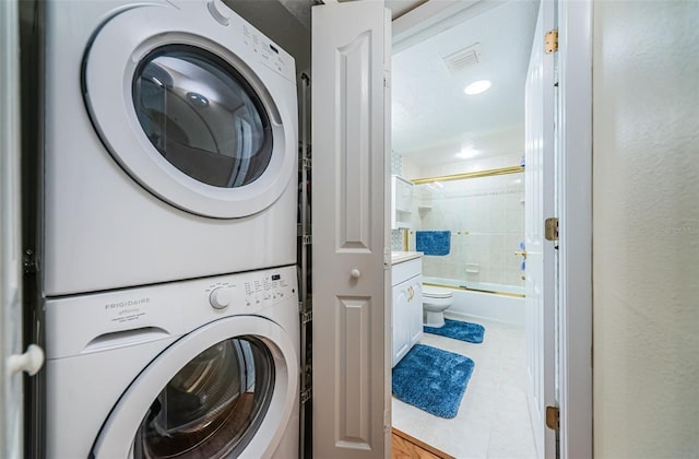 clothes washing area with laundry area, stacked washer and clothes dryer, visible vents, and a textured wall