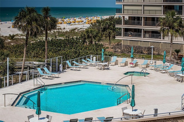 community pool featuring a patio, a beach view, fence, and a water view