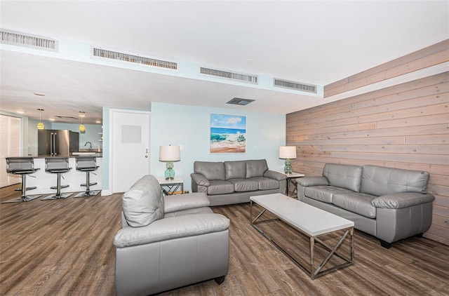 living room with dark wood-type flooring, visible vents, and wood walls