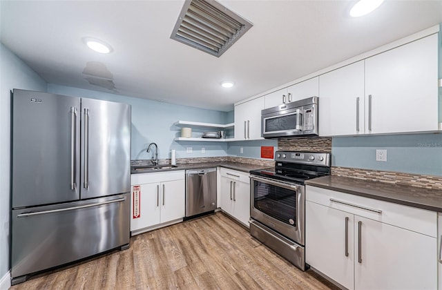 kitchen with open shelves, a sink, light wood-style floors, appliances with stainless steel finishes, and dark countertops