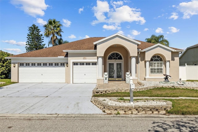 view of front of home featuring french doors, stucco siding, an attached garage, fence, and driveway