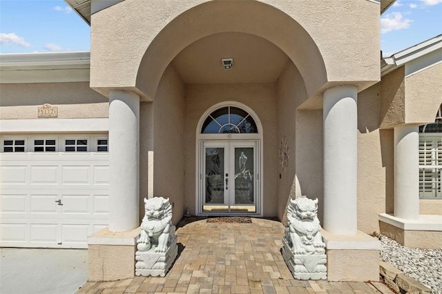 property entrance with a garage, stucco siding, and french doors