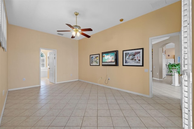 spare room with arched walkways, light tile patterned flooring, ceiling fan, and baseboards