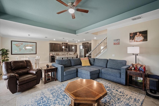 living room featuring a ceiling fan, visible vents, crown molding, and stairs