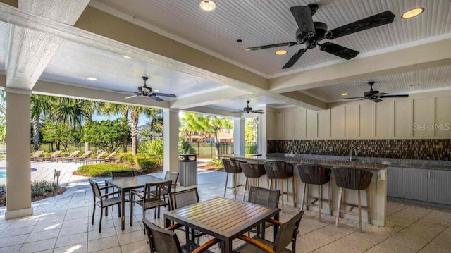 view of patio featuring ceiling fan, outdoor dry bar, fence, a sink, and outdoor dining space