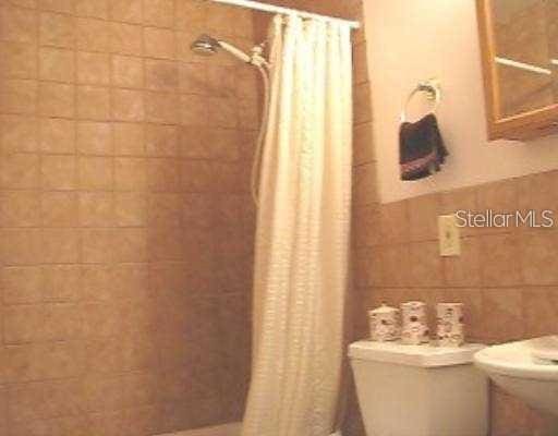 full bathroom with a shower with shower curtain, toilet, and tile walls