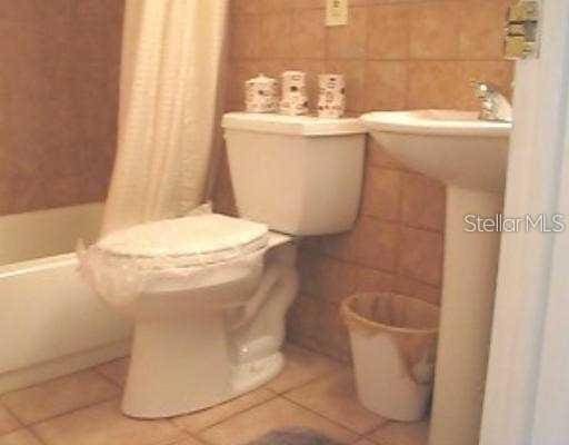 bathroom with curtained shower, tile walls, toilet, and tile patterned floors