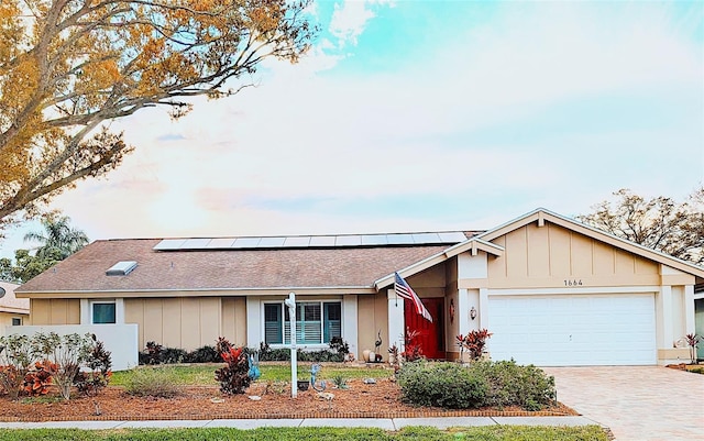 ranch-style home featuring decorative driveway, an attached garage, and roof mounted solar panels