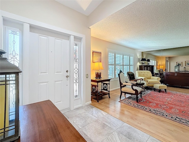 foyer with baseboards, a textured ceiling, and wood finished floors