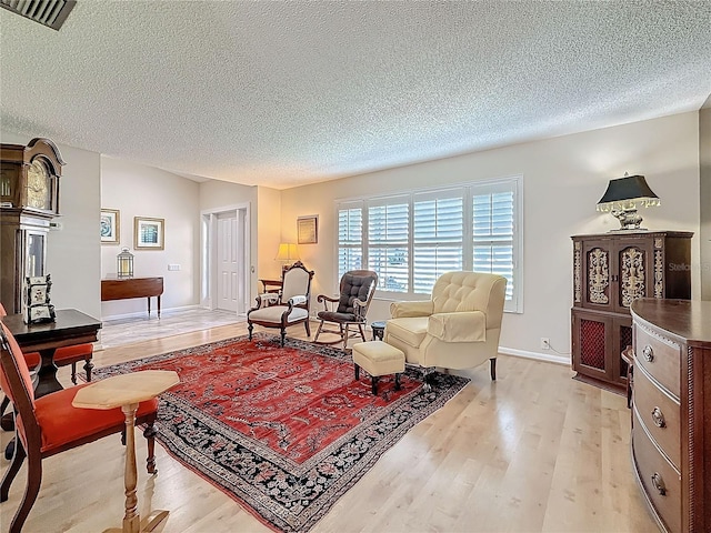 living area featuring light wood-style floors, visible vents, a textured ceiling, and baseboards