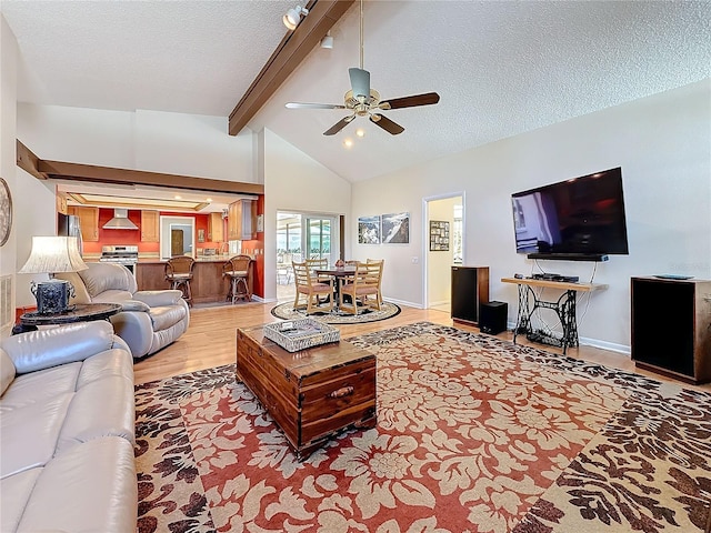 living room featuring vaulted ceiling with beams, a textured ceiling, light wood-style flooring, a ceiling fan, and baseboards