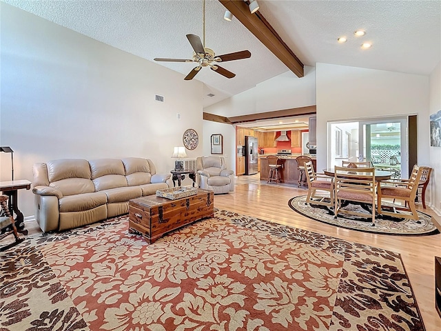 living room with light wood finished floors, a textured ceiling, visible vents, and beam ceiling