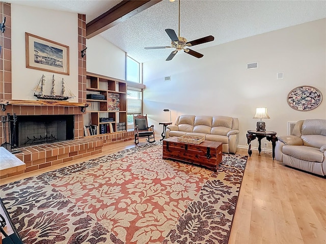 living room with a textured ceiling, a fireplace, wood finished floors, visible vents, and beamed ceiling