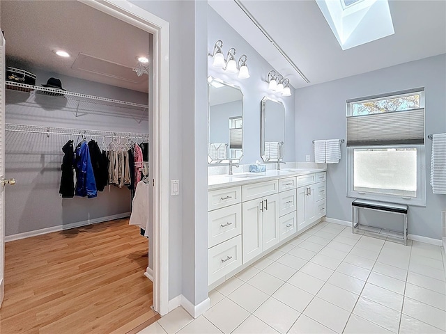 bathroom featuring double vanity, baseboards, a walk in closet, and a sink