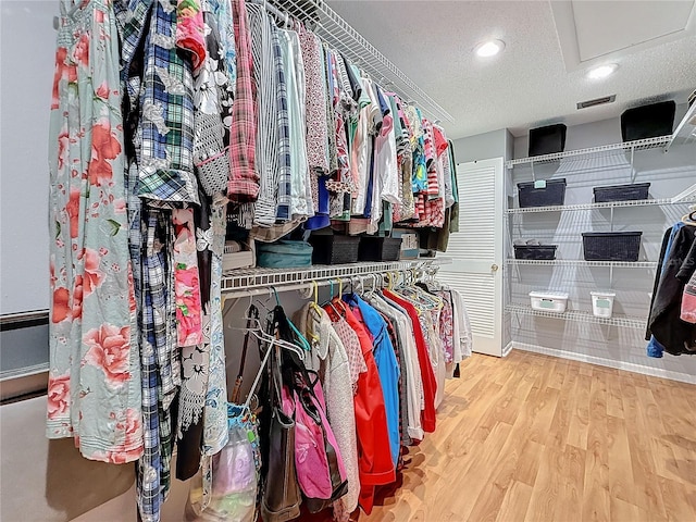 spacious closet featuring wood finished floors, visible vents, and attic access