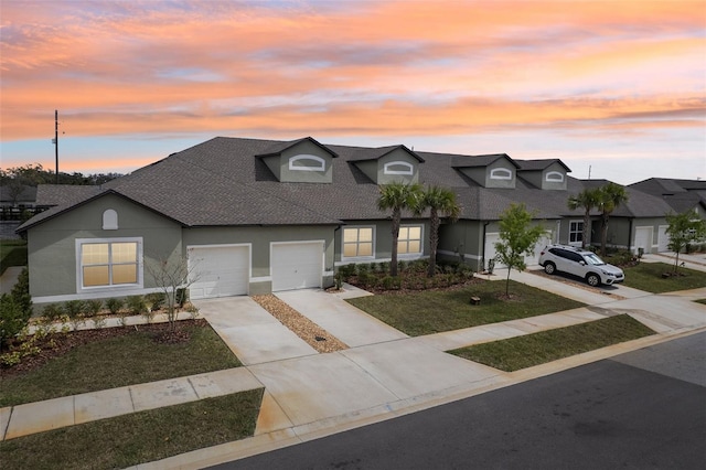 view of front facade featuring a yard, stucco siding, a shingled roof, an attached garage, and driveway