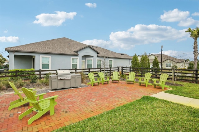 rear view of house with a patio, a shingled roof, fence, and stucco siding