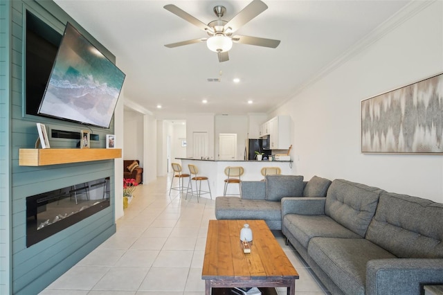 living area featuring light tile patterned floors, visible vents, a glass covered fireplace, crown molding, and recessed lighting