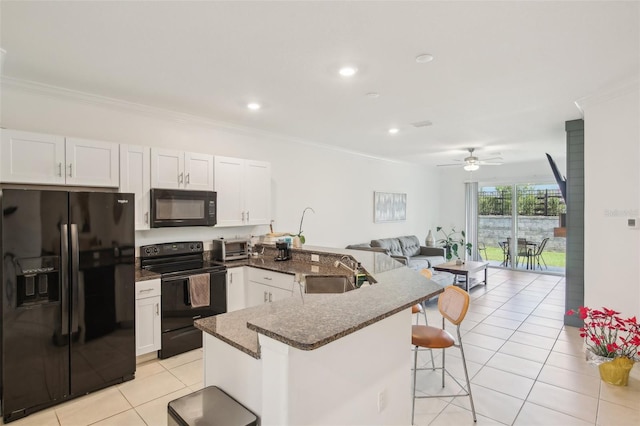 kitchen with a breakfast bar, open floor plan, crown molding, black appliances, and a sink