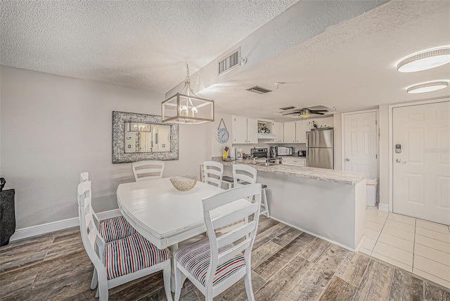 dining room featuring light wood-type flooring, visible vents, a textured ceiling, and ceiling fan