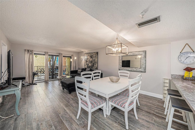 dining space featuring visible vents, baseboards, an inviting chandelier, wood finished floors, and a textured ceiling