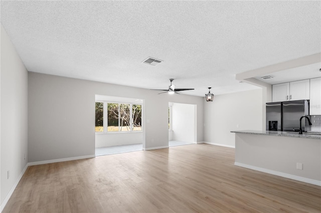 unfurnished living room with a ceiling fan, light wood-type flooring, visible vents, and a textured ceiling