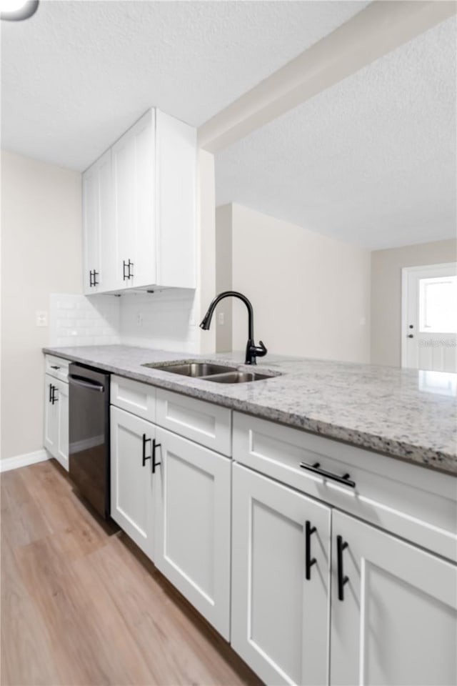 kitchen featuring stainless steel dishwasher, a sink, light stone countertops, and light wood-style floors